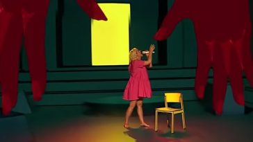 Katy Perry no palco do American Idol cantando Daisies e usando recursos de realidade aumentada: a cantora está em um quarto com longas janelas e um par de mãos desce do teto